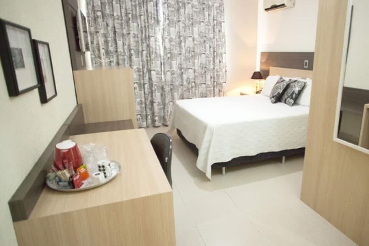 A hotel room with a bed, bedside table, and a desk with a chair.