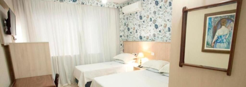 A hotel room with two beds, a wooden chair, a table, and a painting on the wall.