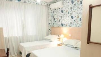 A hotel room with two beds, a wooden chair, a table, and a painting on the wall.