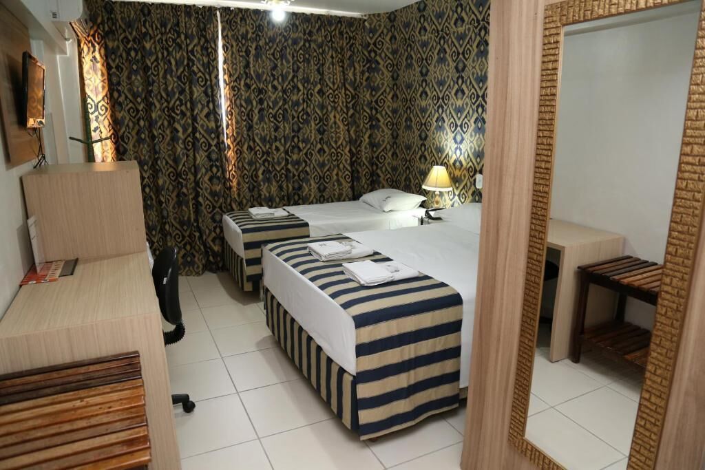 A hotel room with two beds, a desk, a chair, a lamp, and a mirror.