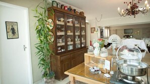 Un coin repas comprenant une table en bois, une table avec un plateau en verre, un plat de service en métal, un buffet avec des portes en verre et une plante en pot.