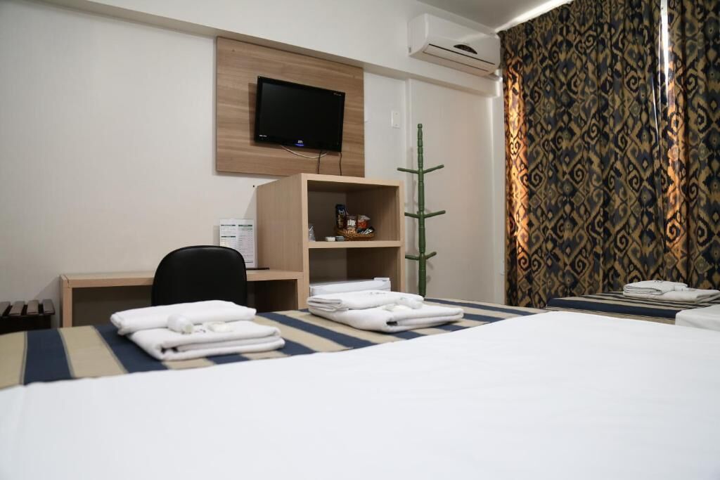 Una habitación de hotel con cama, escritorio, televisor montado en la pared y cortina estampada.