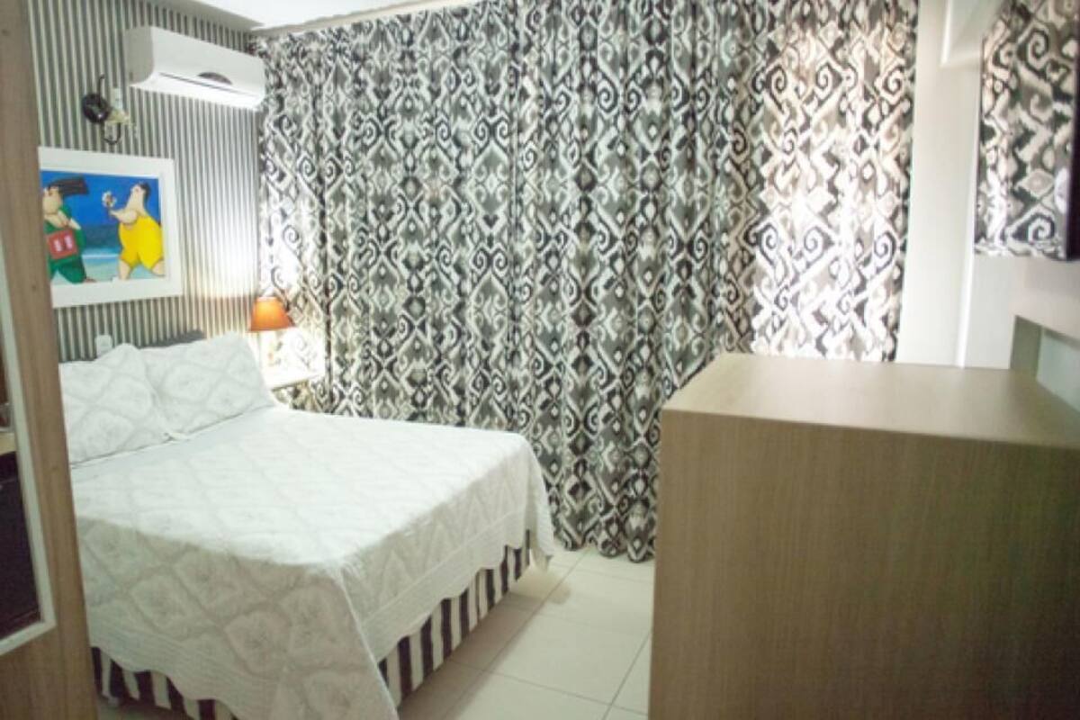 A bedroom with a bed, a dresser, a mirror, and a patterned curtain.