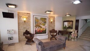 Un salon avec un canapé, une chaise en bois, un tableau, un téléviseur et un escalier.