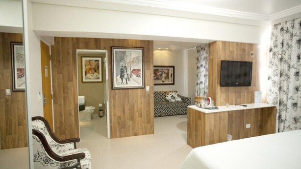 Une chambre d’hôtel avec un lit, un bureau en bois, une télévision et des œuvres d’art encadrées accrochées aux murs.
