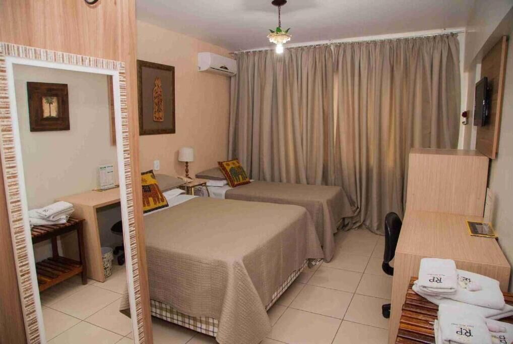 Une chambre d’hôtel avec deux lits, un bureau avec une lampe, une chaise, une télévision et un miroir.