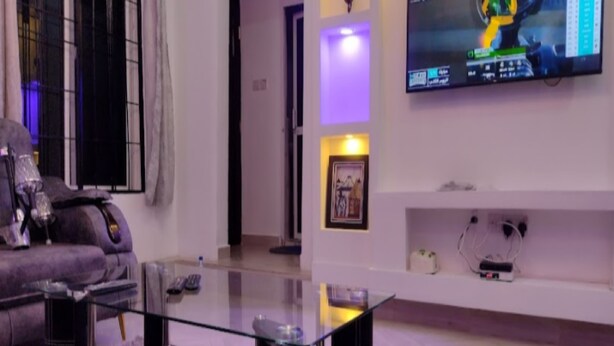 Een moderne woonkamer met een glazen salontafel, een bank en een flatscreen tv aan de muur.