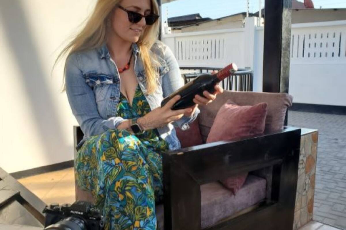 Une personne est assise sur un canapé, un ordinateur portable est posé sur ses genoux et un appareil photo se trouve sur le sol à côté d’elle.