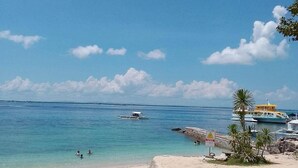 Une plage à l’eau turquoise et limpide, quelques bateaux et une petite construction surmontée d’un toit jaune.