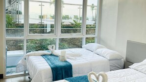 Une chambre d’hôtel avec deux lits, de grandes fenêtres et une vue sur une piscine et des palmiers.