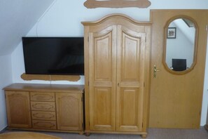 A room with a wooden wardrobe, a television on a stand, and a door with a mirror.