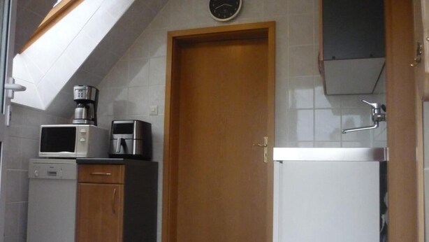 A compact kitchen with a microwave, coffee maker, dishwasher, and a wooden door. - Apartment Storchennest upper floor (Kramerhof)