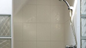 A bathroom with white tiles, a black and white border, and a shower with a handheld showerhead. - Apartment Storchennest upper floor (Kramerhof)
