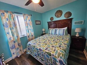 A bedroom with a bed, curtains, a nightstand, a lamp, and wall decorations.