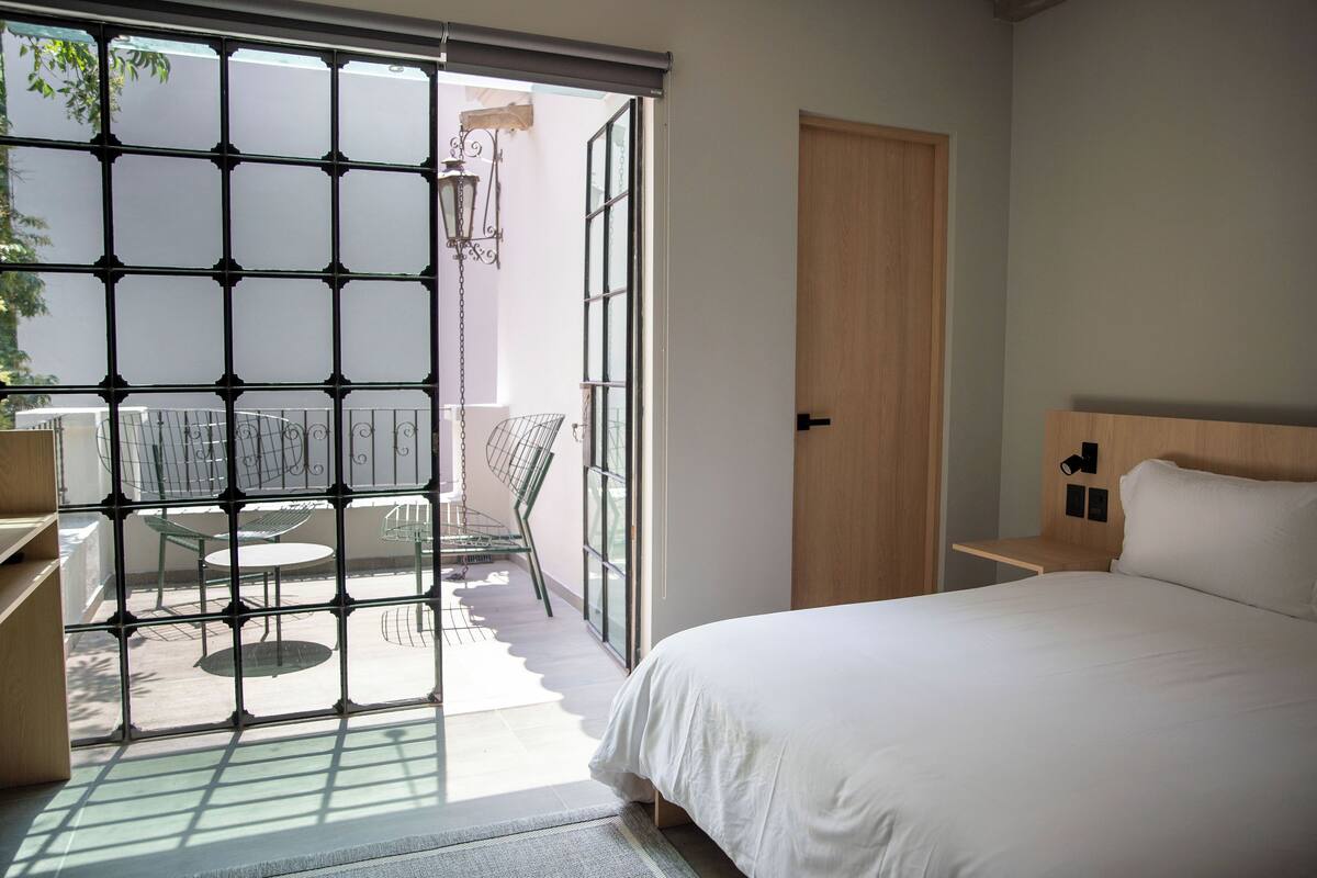 A bedroom with a bed, a wooden door, and a view of an outdoor patio with chairs and a table.