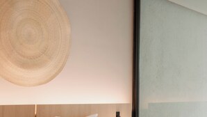 A modern hotel room with a large bed, a round woven headboard, a bedside table with a lamp, and a view of the outside through a large window. - Casa Lomah Napoles WTC (Mexico City)