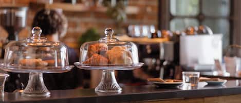 A bakery counter with pastries under glass domes, a brick wall, and a window in the background.