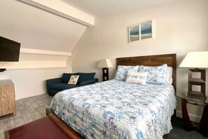 Um quarto com cama, sofá, televisão e uma mesinha.