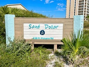 A sign for 'Sand Dollar' at 336 Ft Pickens Rd, surrounded by greenery and a clear sky. - Sand Dollar W204 Inexpensive Bayfront Escape! 2,3 & 4-Night Getaways (Pensacola Beach)