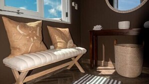 Una habitación con un banco, un espejo redondo, una mesita y un cubo de basura.