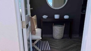 Una puerta que da a una habitación con piso de parquete, un espejo en la pared y un felpudo.