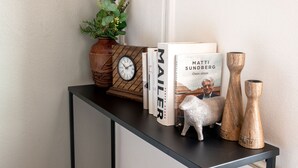 Una consola con un reloj, libros, una oveja decorativa y jarrones de madera.