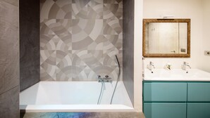 A modern bathroom with a geometric patterned wall, a white bathtub, and a teal vanity with a mirror. - Closed structure, not existing (Potenza)