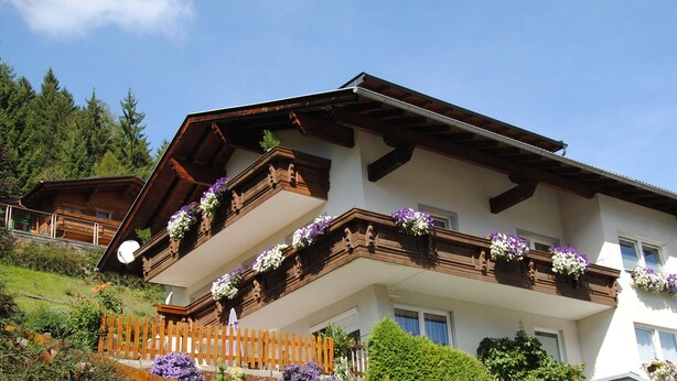 A two-story chalet with wooden balconies, a wooden fence, and a garden with flowers. - holiday apartment Serlesblick (Fulpmes)
