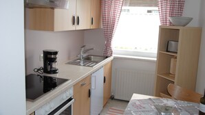 A compact kitchen with a stove, sink, and a coffee maker. There is a window with checkered curtains and a radiator below. - holiday apartment Serlesblick (Fulpmes)