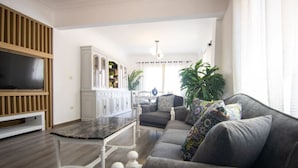 A living room with a sofa, a TV, a dining table, and a kitchen area with cabinets. - Lovely 3BR Apartment in Heart of Mohandseen (Giza Governorate)