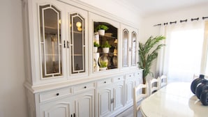 A dining area with a white table and chairs, a large cabinet with glass doors, and a potted plant. - Lovely 3BR Apartment in Heart of Mohandseen (Giza Governorate)
