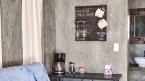 A modern living room with a grey sofa, a coffee table, and a wall-mounted sign with kitchen items. - SUEÑA@TierraAmada-in the heart of the valley 1OF7 (Guadalupe, Ensenada)
