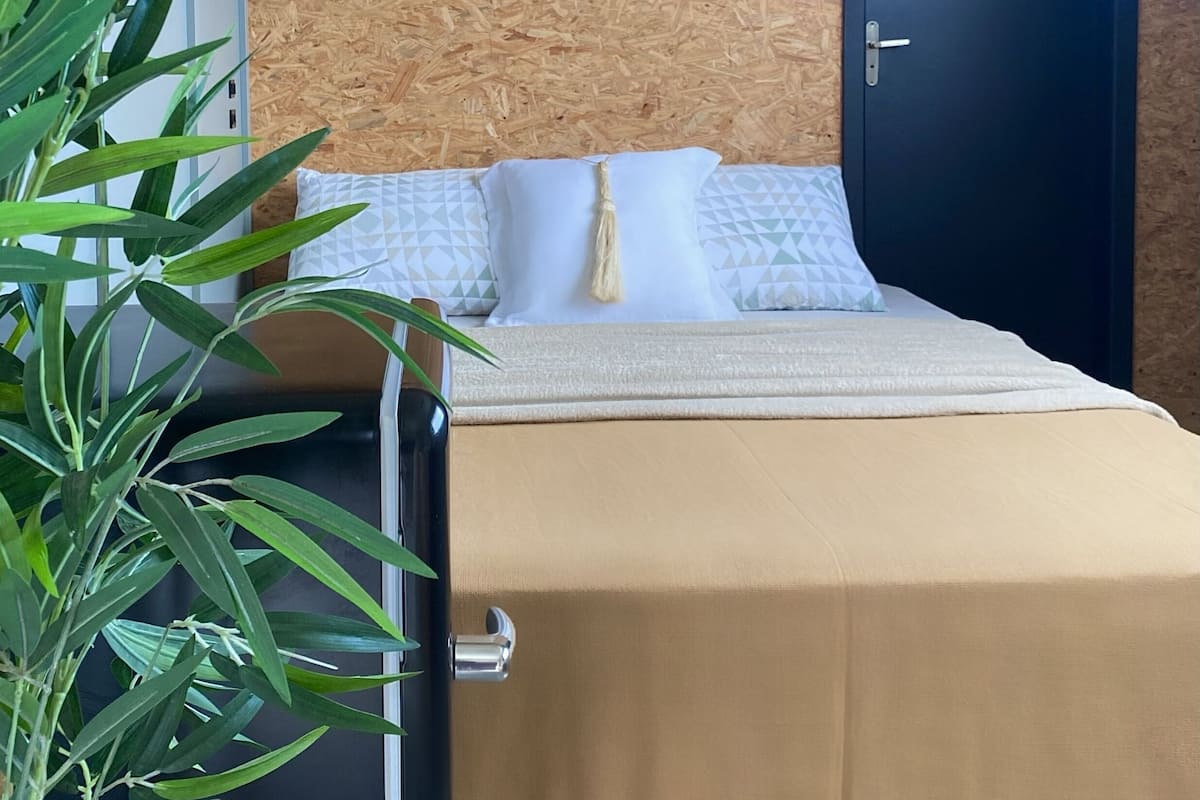 Une chambre avec un lit, une décoration murale en macramé, une porte sombre et une plante en pot.