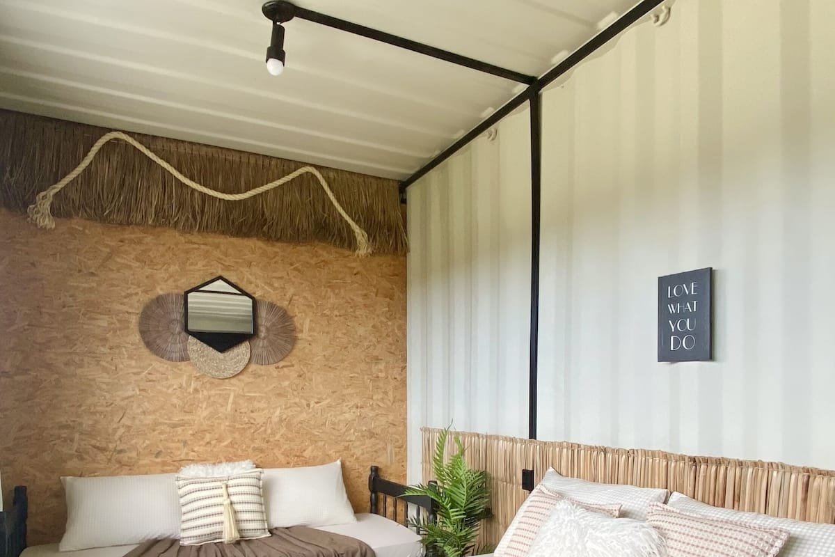 Une chambre d’hôtel avec deux lits, un mur décoratif en bois, un luminaire suspendu et une citation inspirante sur le mur.