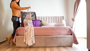 Una habitación con una cama, una maleta y ropa colgada.