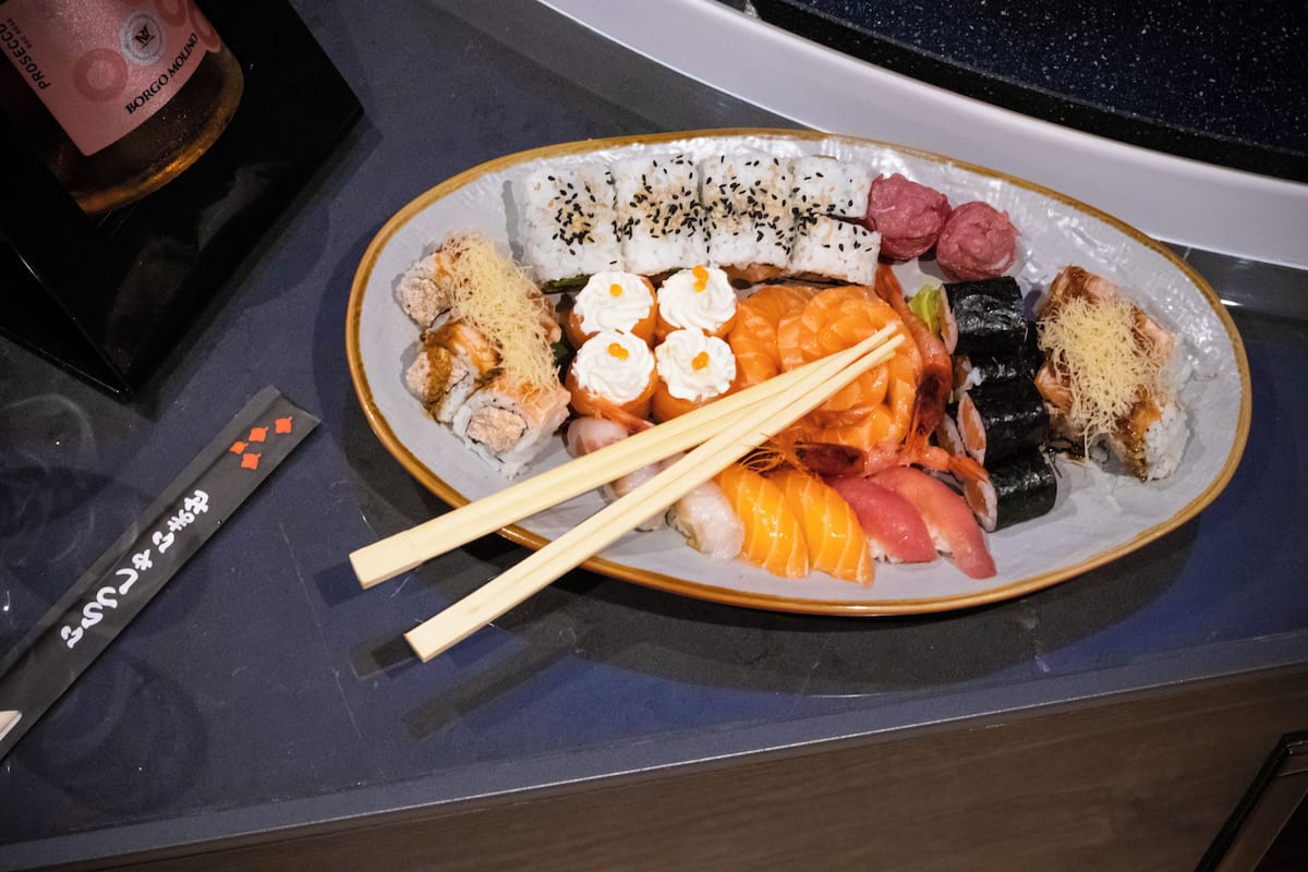 A plate of sushi with chopsticks and a remote control on a table.