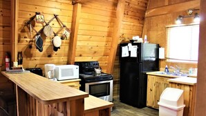 Una cocina pequeña con paredes de madera, un horno, un microondas, un refrigerador y un lavamanos.