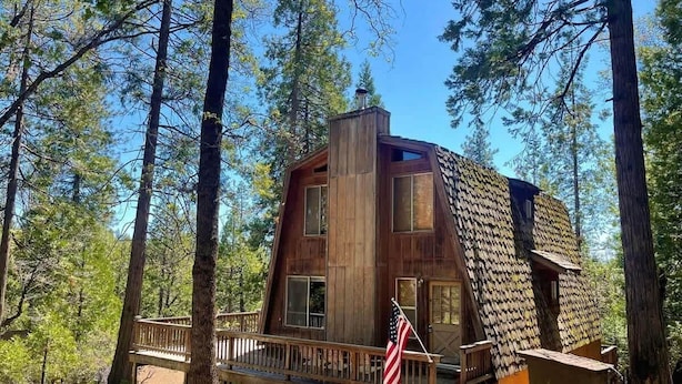 Una cabaña de madera con terraza y una bandera estadounidense, rodeada de árboles.