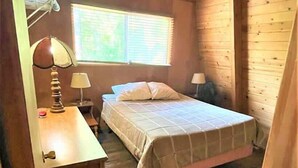 Un dormitorio de cabaña de madera con cama, mesitas de noche y una ventana.