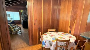 A wooden interior with a round table covered in a floral tablecloth, surrounded by wooden chairs.