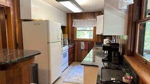A compact kitchen with wooden cabinets, a refrigerator, a stove, and a coffee maker.