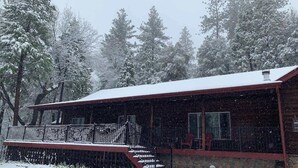 Une cabane dotée d’un porche abrité et de fondations en pierre, entourée d’arbres couverts de neige.