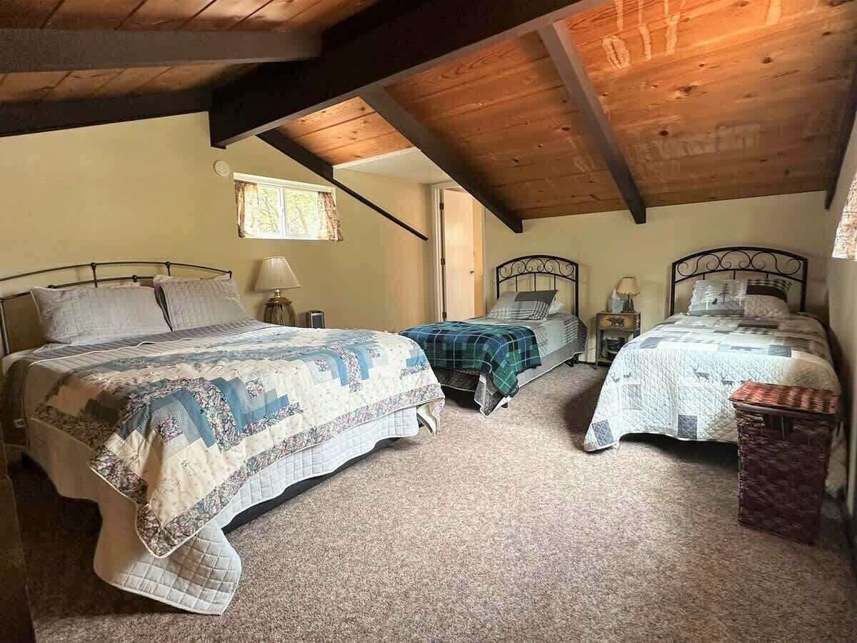 Ein Schlafzimmer mit drei Betten, Holzbalkendecke und einem kleinen Fenster.