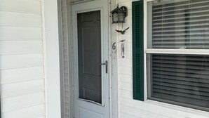 A white door with a glass panel, a window with green shutters, and a small outdoor vent.