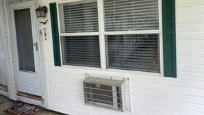 A white house with green shutters, a door, and a window with a vent below it.