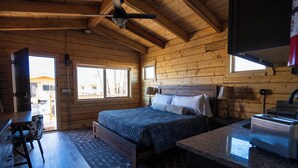 A wooden cabin bedroom with a bed, a desk, and a window. - Muddy Creek Mining Company (Hanksville)