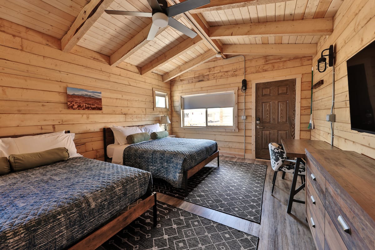 A wooden cabin with two beds, a desk, and a ceiling fan.