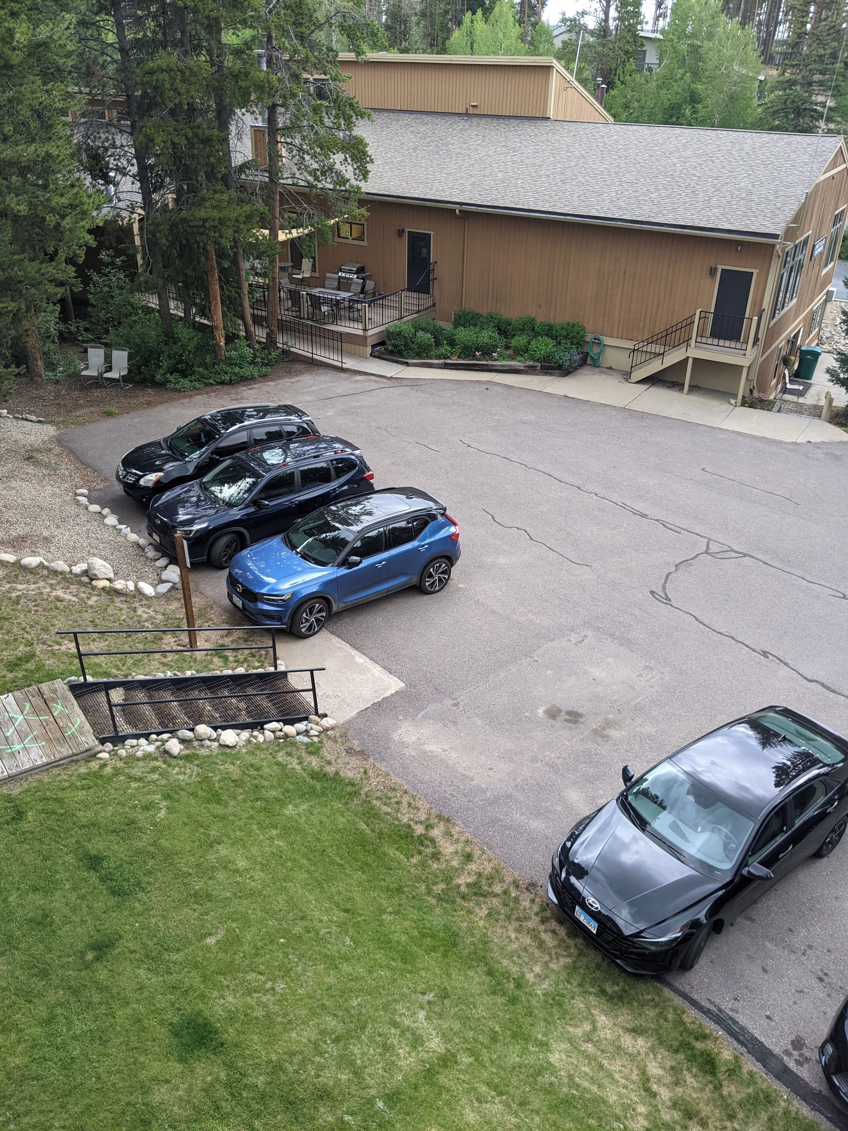 A parking lot with several cars, a building with a sloped roof, and a staircase leading to a second floor.
