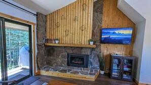 Ein Wohnzimmer mit Kamin aus Stein, Holzwand, Fernseher und Bücherregal.