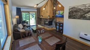 Ein gemütlicher Wohnbereich mit Kamin aus Stein, Holzbalkendecke und großem Fenster mit Blick auf einen Wald.